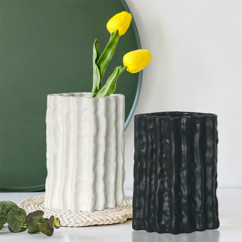 Two textured vases, one white and one black, with yellow tulips on a light background.