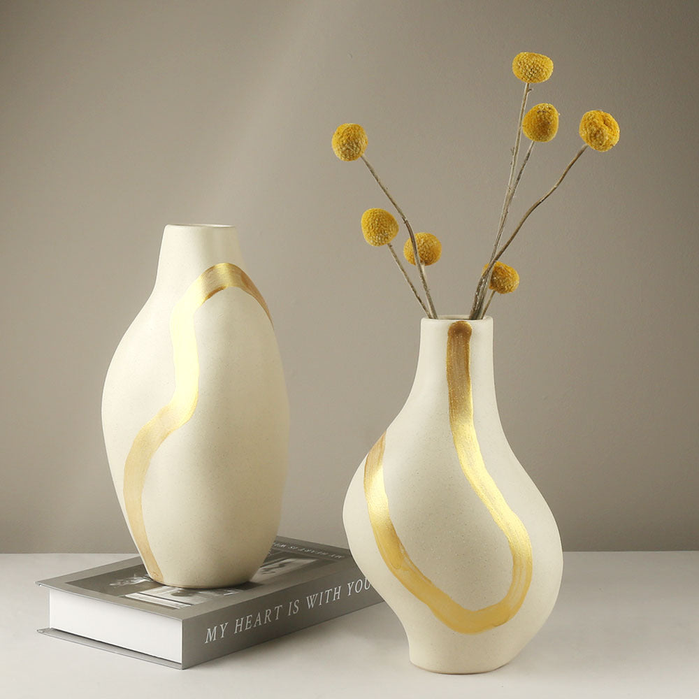Two white vases with gold accents, one holding yellow flowers, on a neutral background.