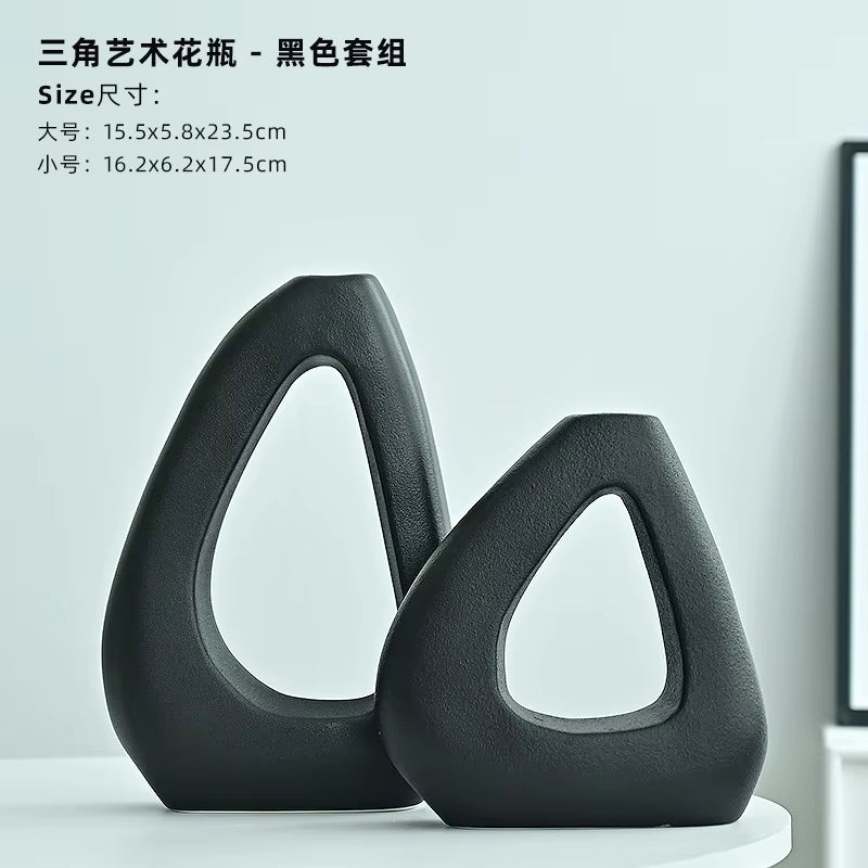Two black artistic vases on a white surface with a light gray background