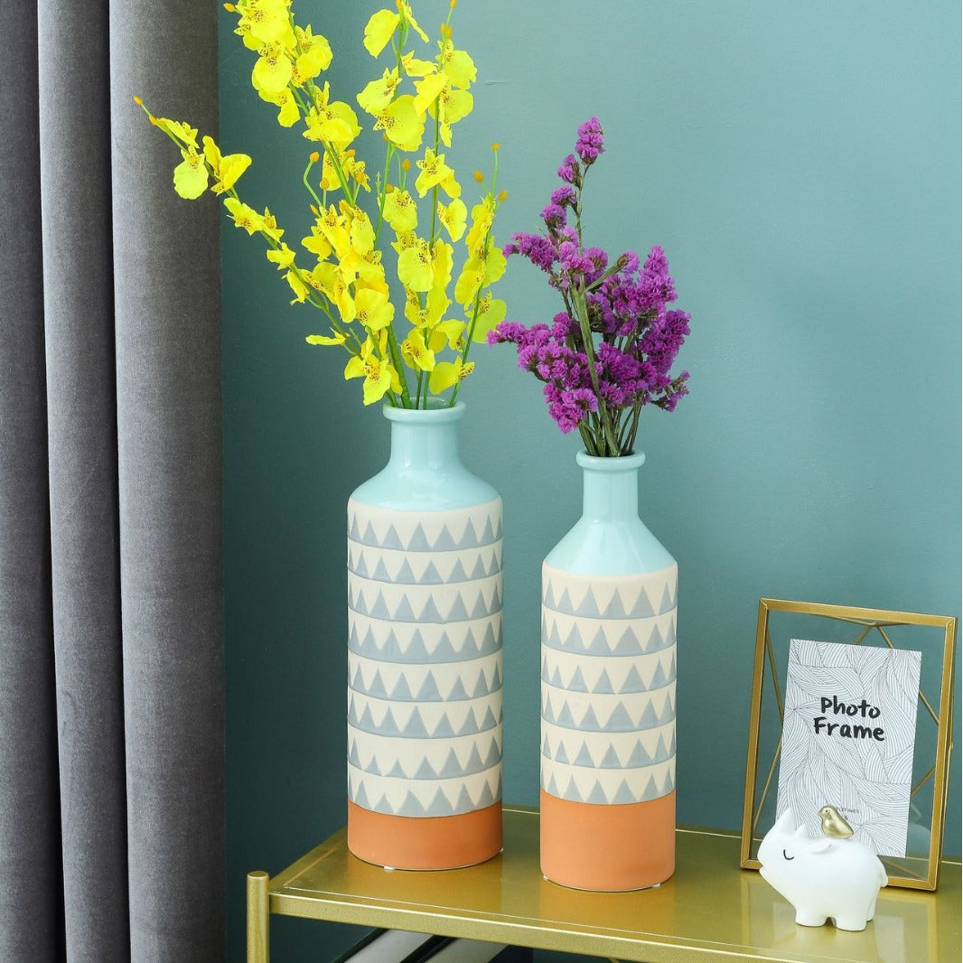 Two decorative vases with geometric patterns on a shelf against a teal wall.