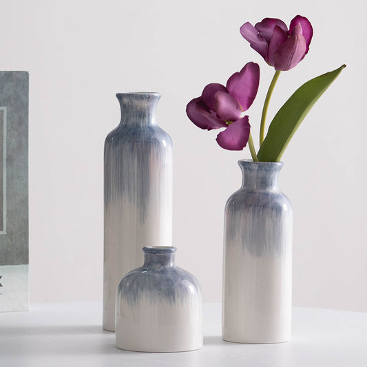 Two ceramic vases with gradient blue and white design, one containing purple tulips on a light background.