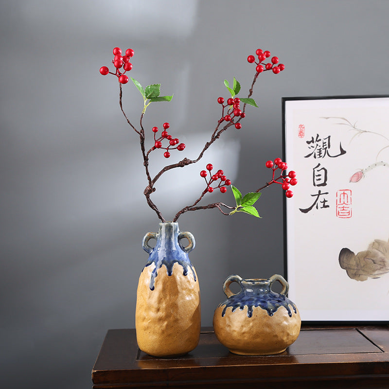 Two ceramic vases with blue glaze on a wooden surface with a framed artwork in the background.
