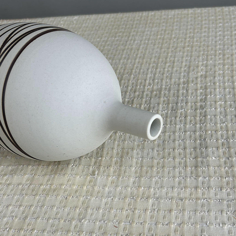 White ceramic vase with black stripes on a textured surface