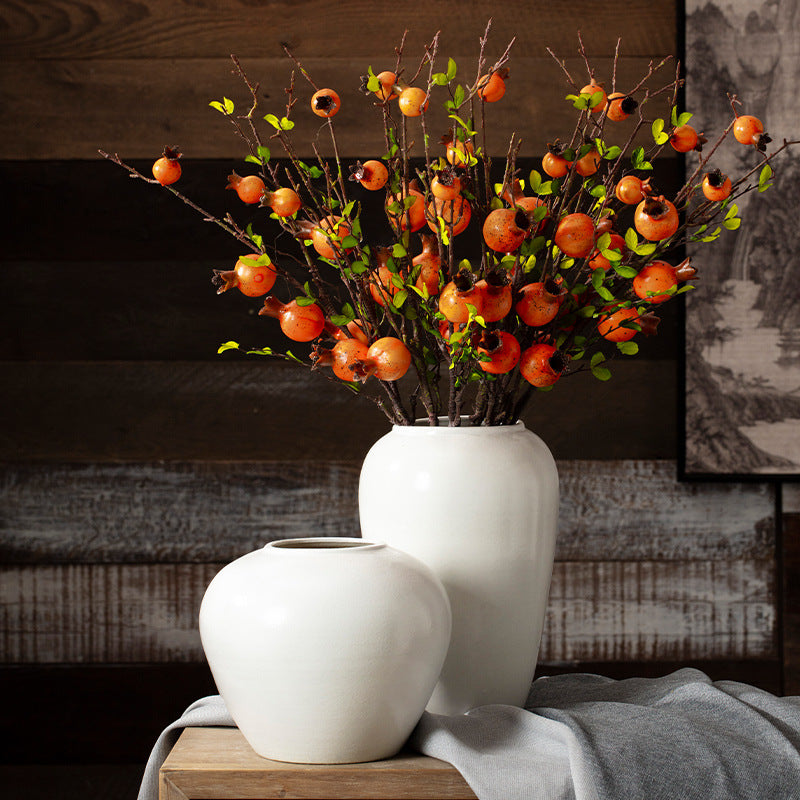 White vases with decorative branches and fruits on a wooden surface.