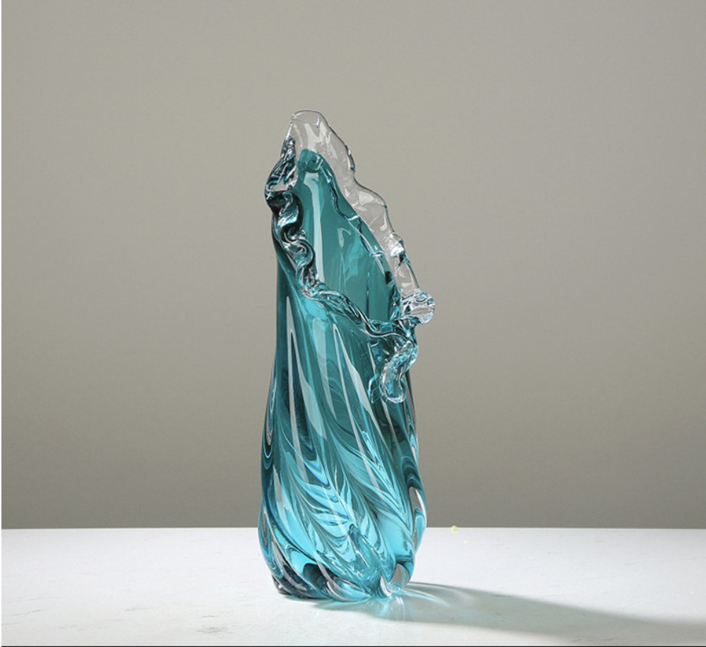 Turquoise glass sculpture on a white surface with a gray background