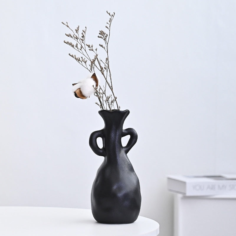 Black vase with dried branches on a white surface against a light gray background