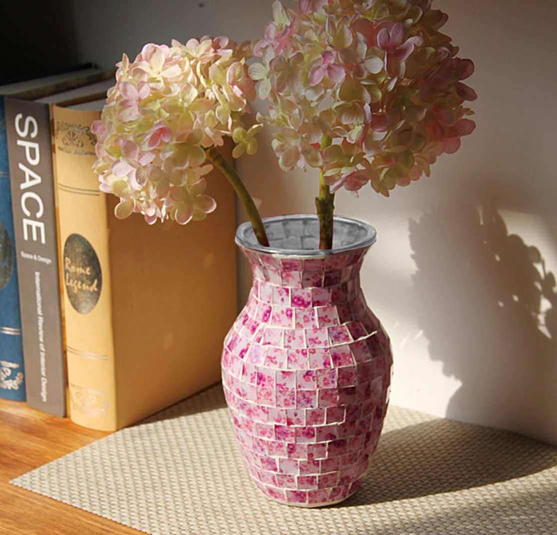 Pink mosaic vase with flowers on a table next to books