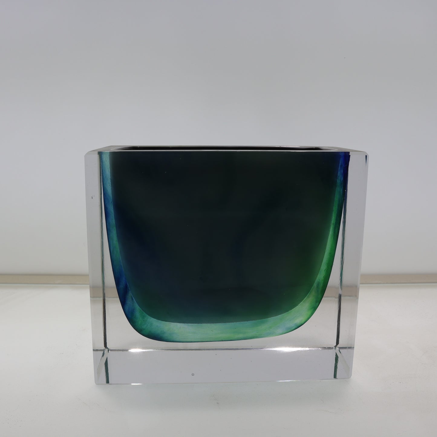 Clear glass vase with a greenish-blue gradient on a white background