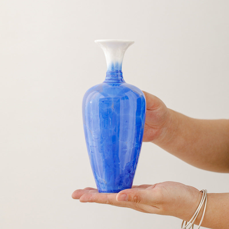 Blue and white ceramic vase held by a hand on a light background