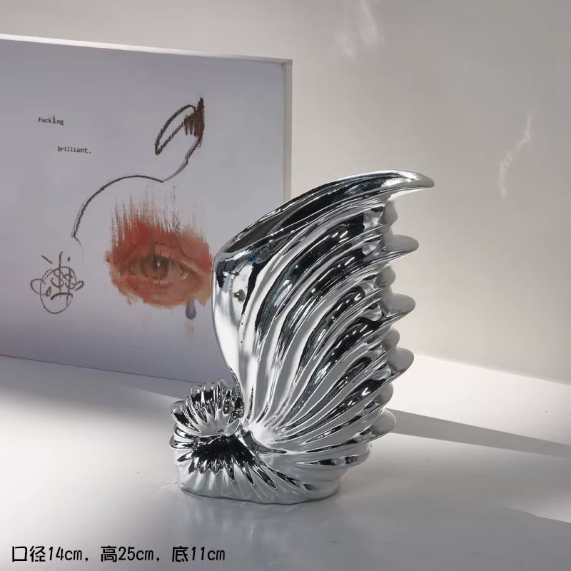 Silver abstract sculpture on a white surface with a blurred artwork in the background