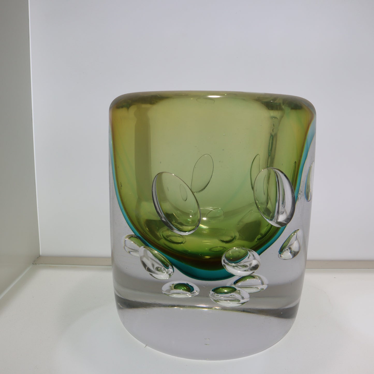 Green and clear glass vase on a white surface with a white background