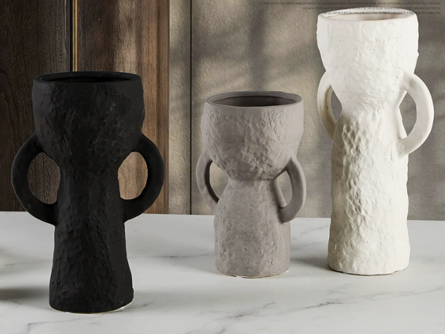 Three textured vases in black, gray, and white on a marble surface with a wooden wall background.