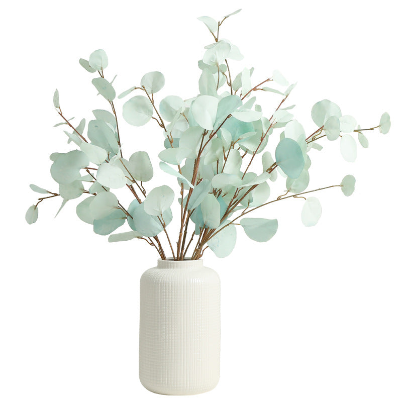 Faux eucalyptus branches in a white vase on a white background