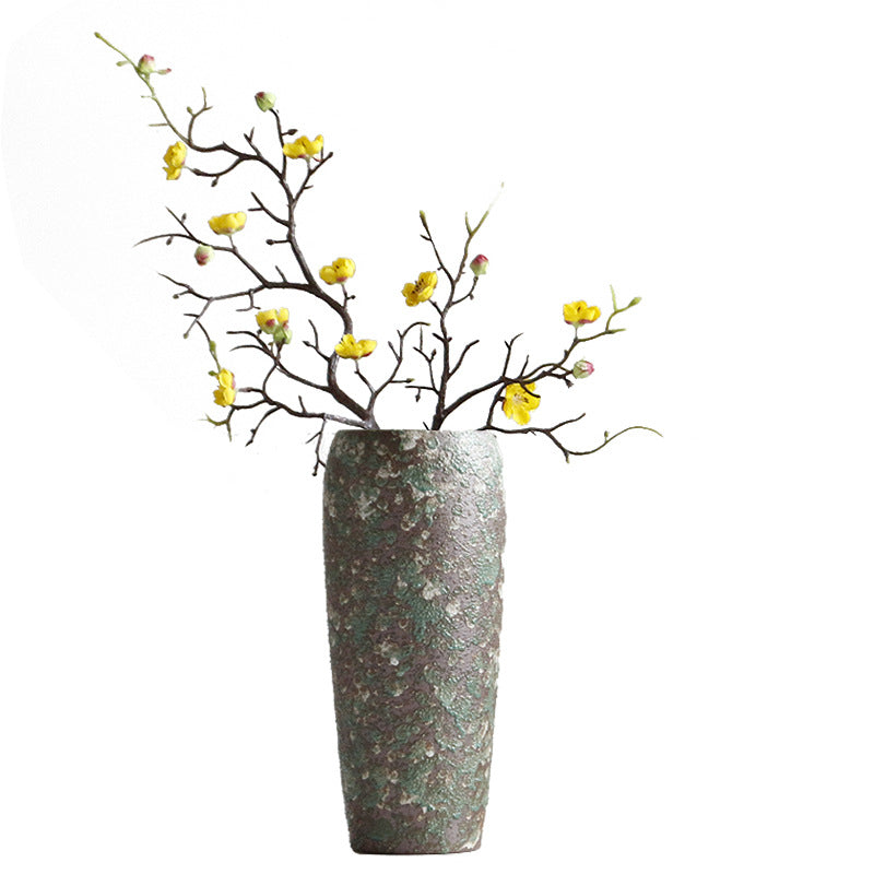 Decorative vase with textured surface holding branches with yellow flowers on a white background