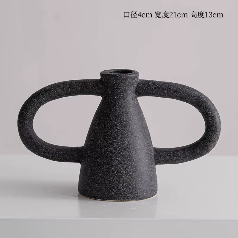Black ceramic vase with dual handles on a light gray background