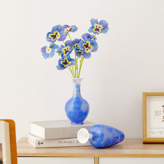 Blue vase with flowers on a wooden shelf against a white wall