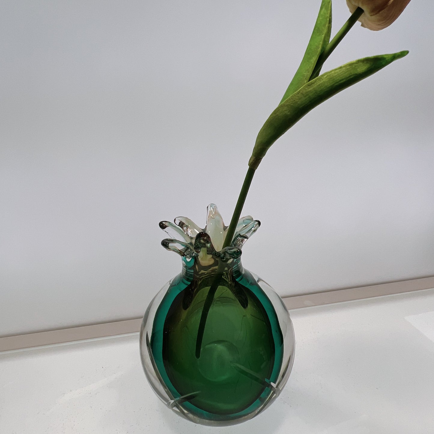 Green glass vase with a single flower on a white surface