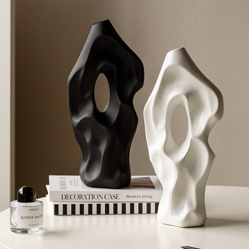 Two abstract sculptures, one black and one white, on a surface with books and a perfume bottle.