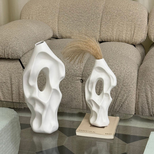 Two abstract white vases on a glass table with a beige sofa in the background