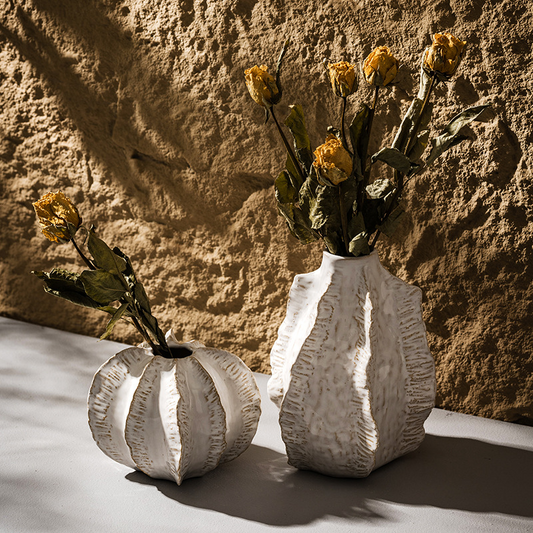 Two textured vases with dried flowers against a stone wall.
