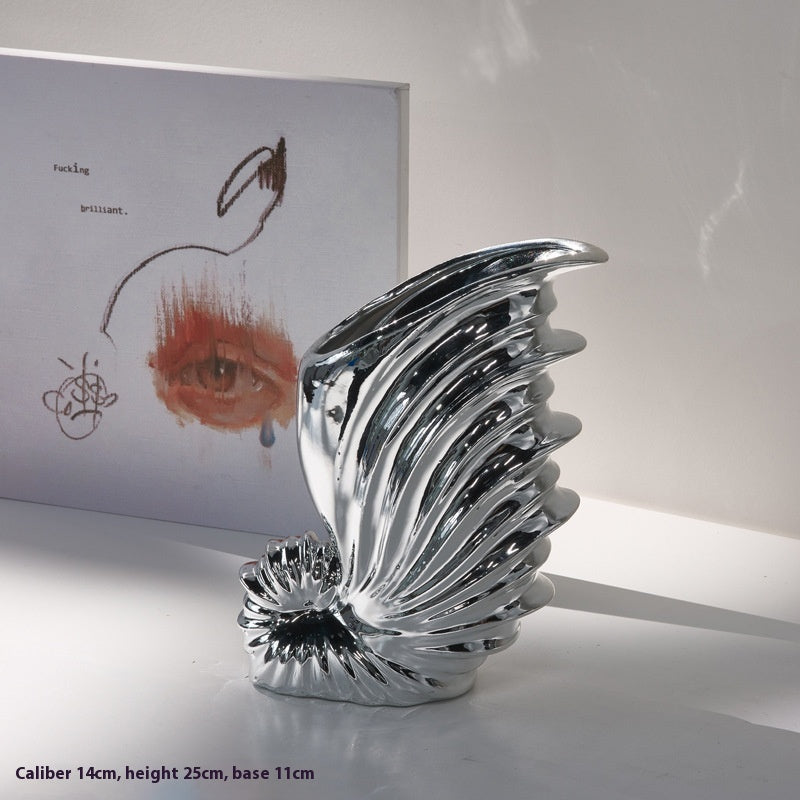 Chrome shell-shaped object on a white surface with a blurred background