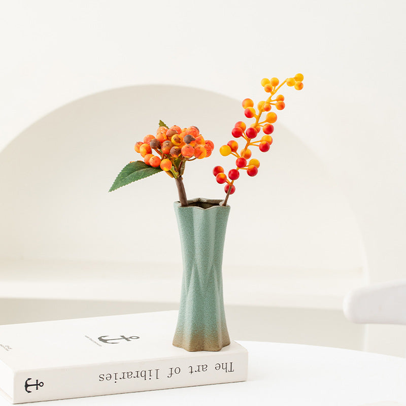 Small green vase with decorative plants on a white surface