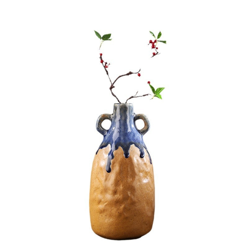 Ceramic vase with a blue top and brown body, containing branches with leaves and berries on a white background.