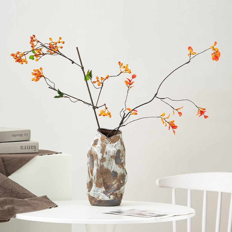 Decorative vase with branches and orange flowers on a white surface