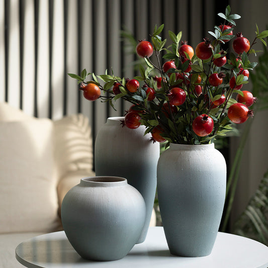 Three light blue vases with a bouquet of red apples and green leaves on a table.