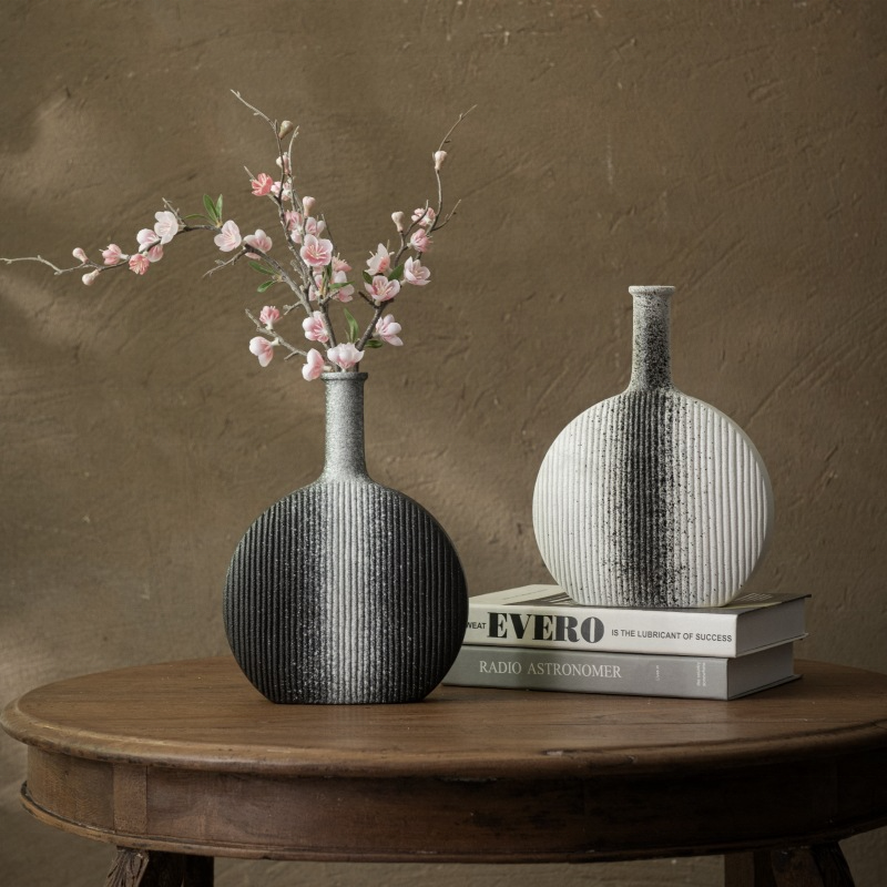 Two textured vases on a wooden table with a book and floral arrangement against a brown background