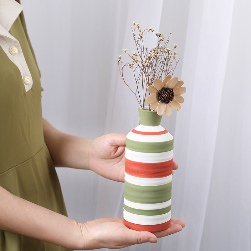Person holding a striped ceramic vase with flowers against a white background