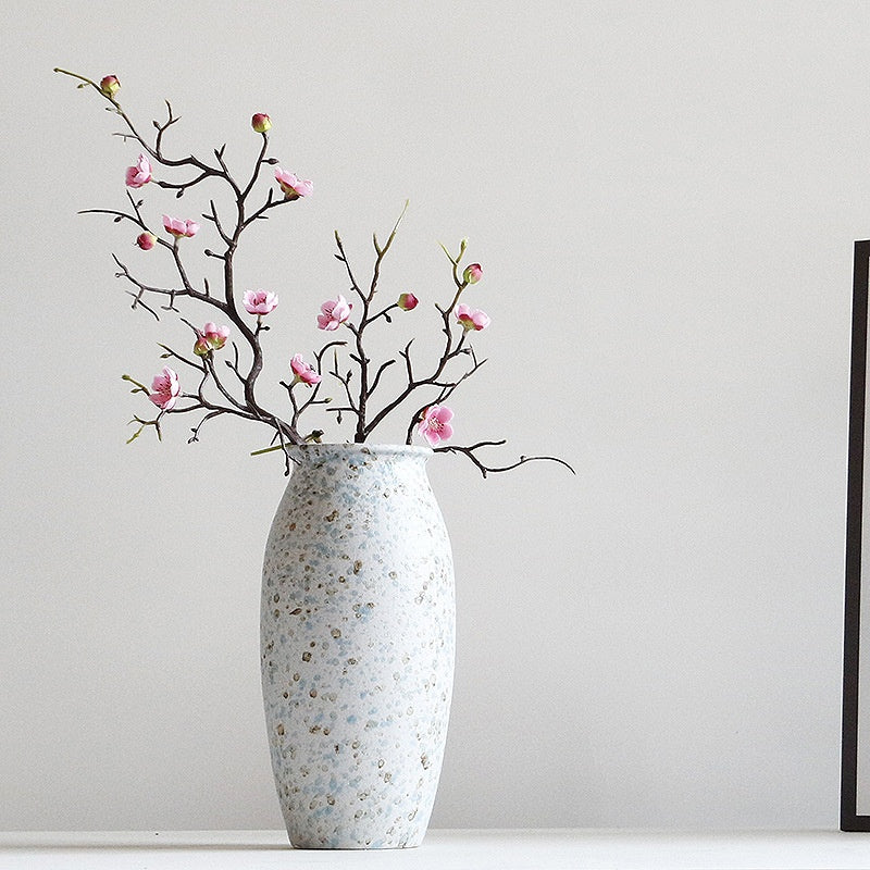 Decorative vase with speckled pattern and floral branch against a plain background