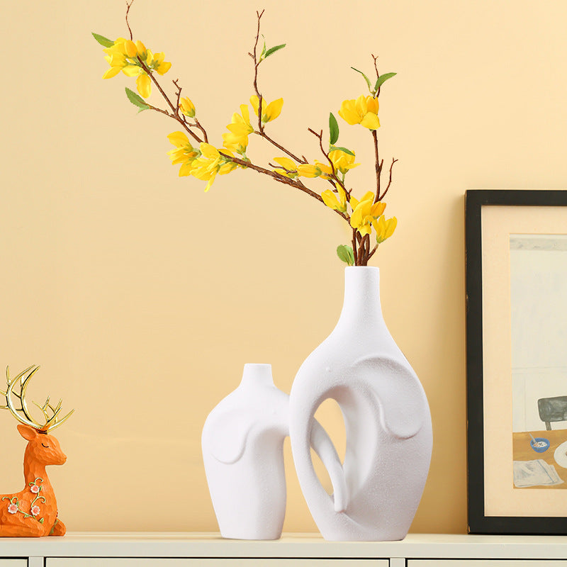 Decorative scene with white vases, a yellow flower arrangement, and a deer figurine on a beige wall background.