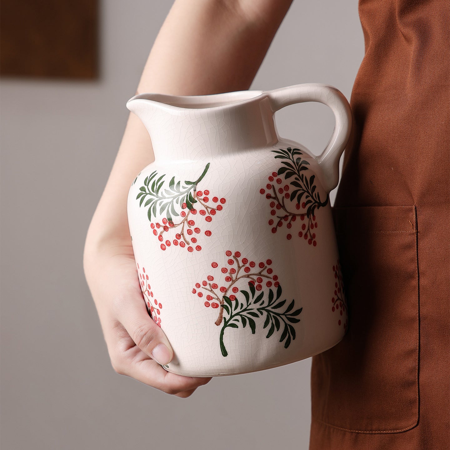 Person holding a white ceramic pitcher with floral patterns on a neutral background