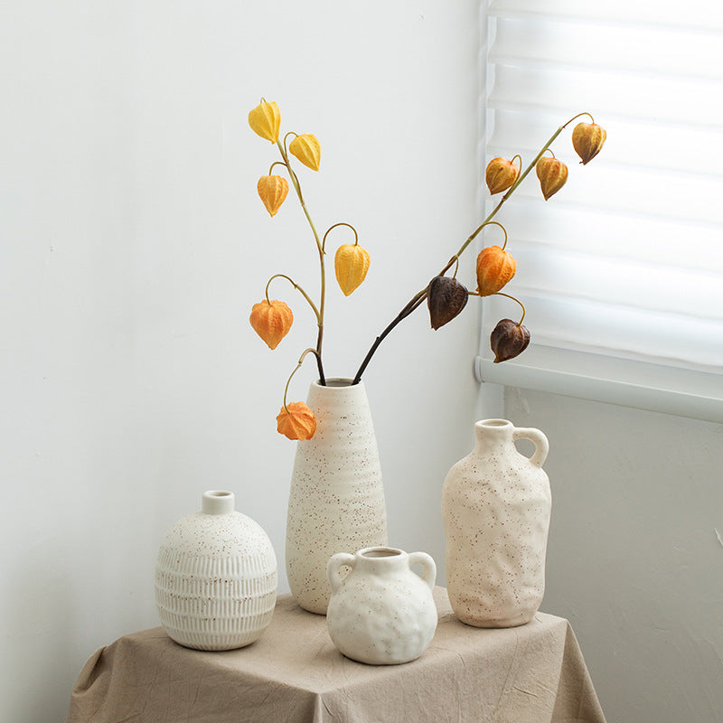Set of four ceramic vases with textured surfaces on a table against a white wall.