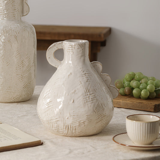 White textured ceramic pitcher on a table with grapes and a notebook in the background