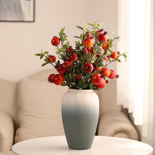 Vase with artificial pomegranate branches on a table in a room setting