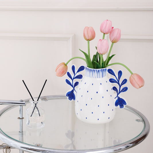 White vase with blue floral patterns containing pink tulips on a glass table.
