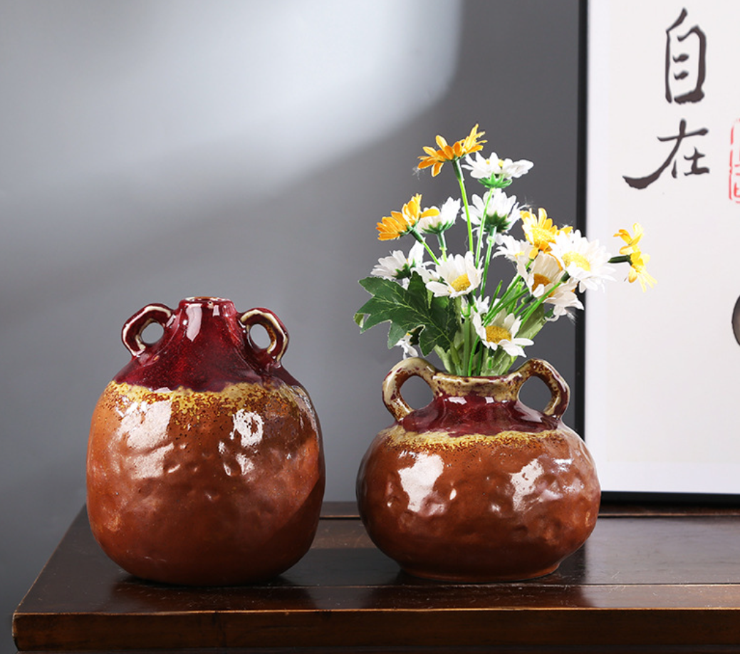 Two ceramic vases with handles on a wooden surface, one containing flowers.