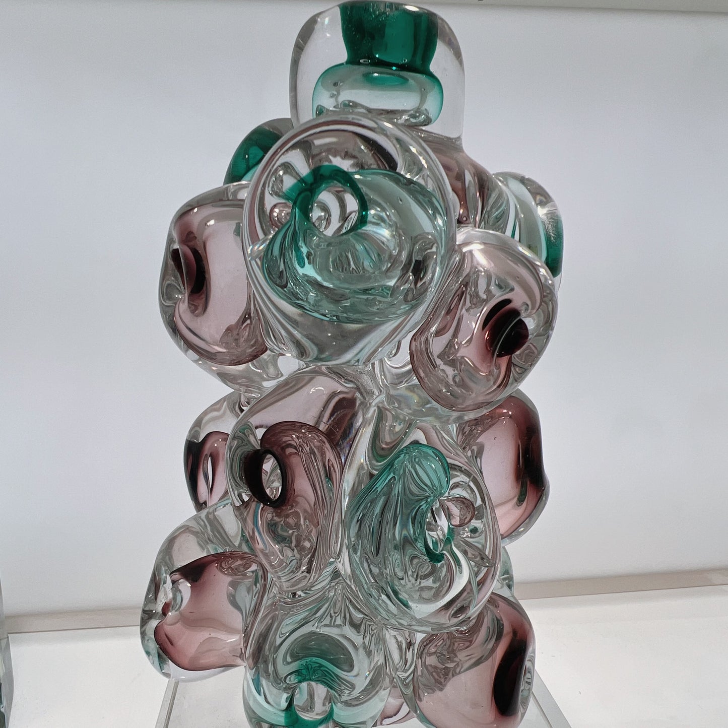 Glass sculpture with swirl patterns in green, clear, and pink on a white background