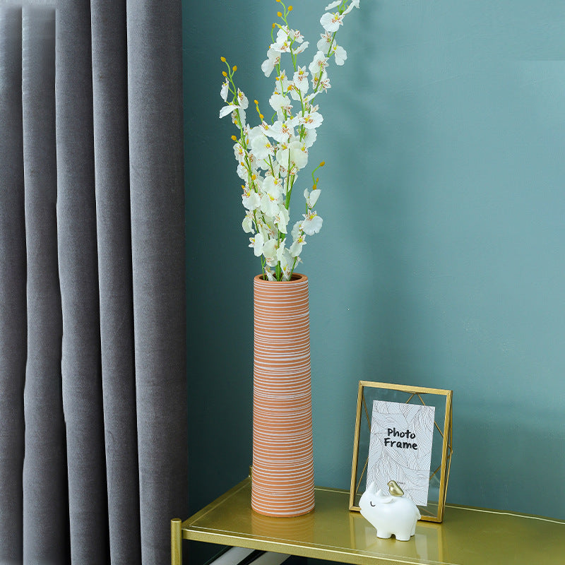 Tall cylindrical vase with white flowers on a green shelf against a teal wall.