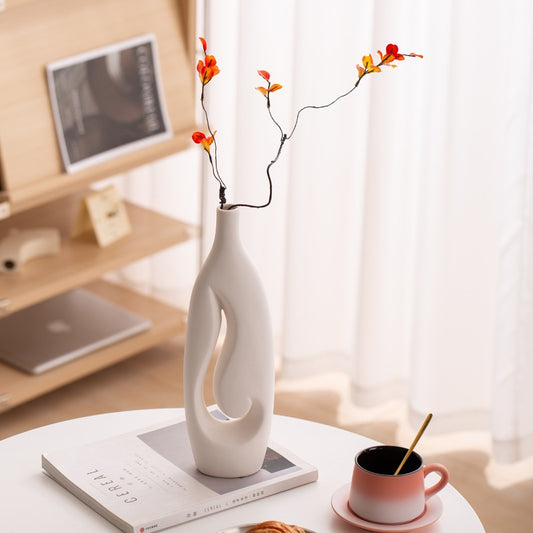 White ceramic vase with decorative branches on a table in a home office setting