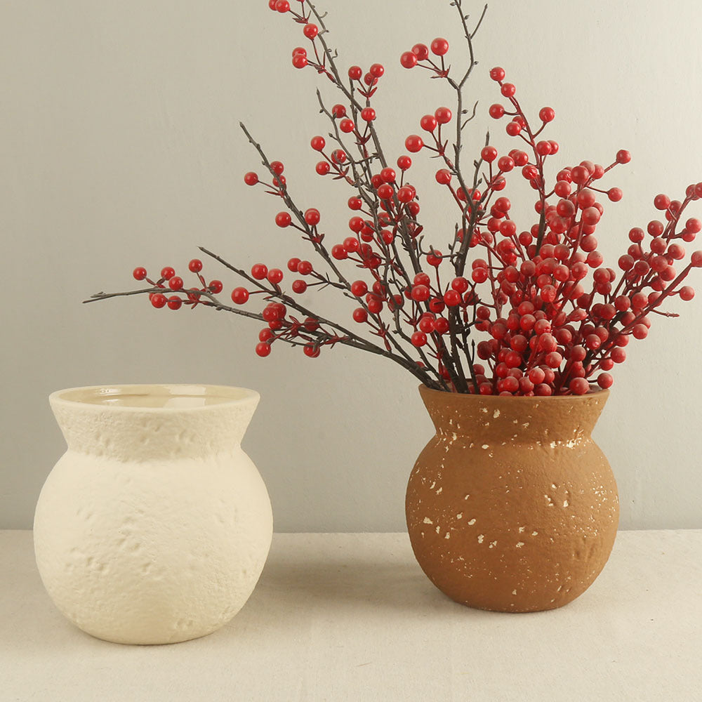 Two ceramic vases, one white and one brown speckled, with red berry branches on a neutral background.