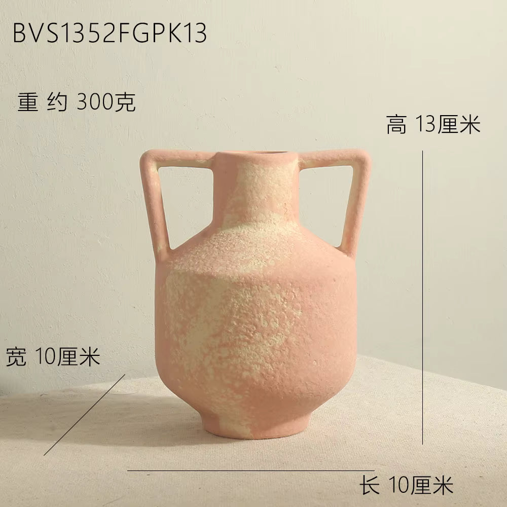 Pink ceramic vase with handles on a beige surface and light gray background