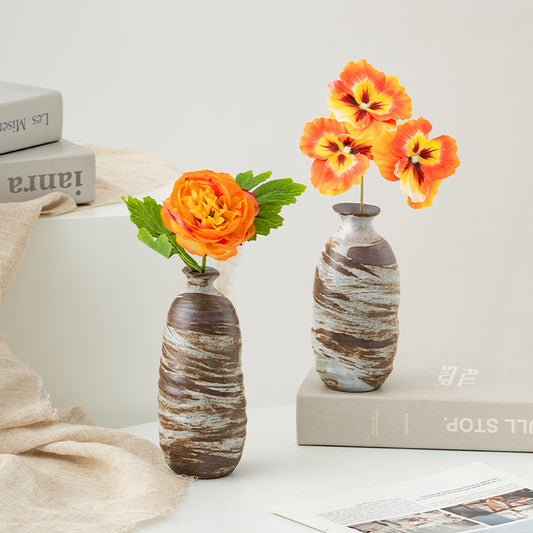 Two decorative vases with orange flowers on a light surface with books in the background.