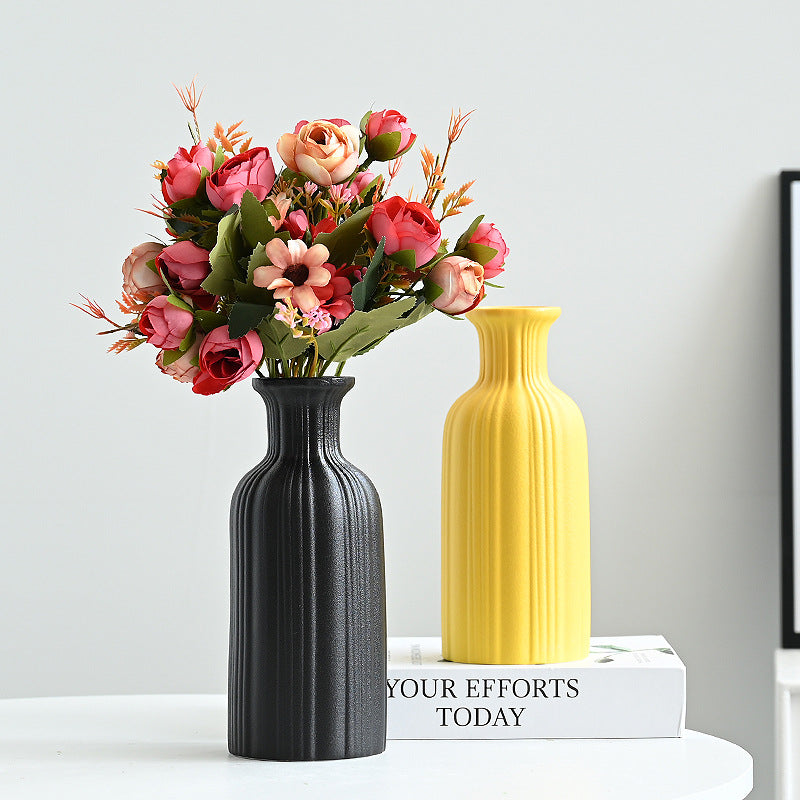 Two vases, one black and one yellow, with a bouquet of flowers on a white surface.