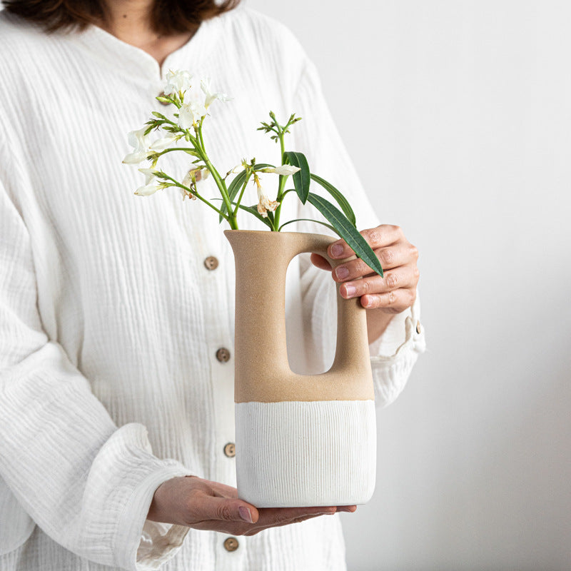 Person holding a two-toned ceramic vase with flowers against a plain background