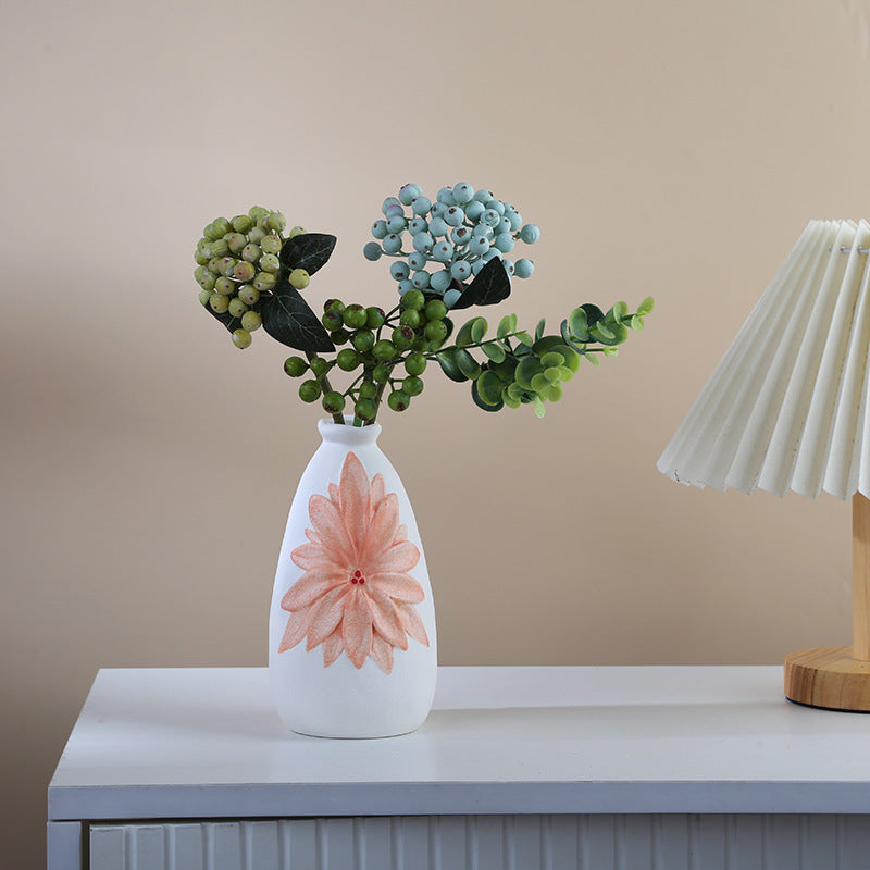 White vase with a pink flower design on a table against a beige wall