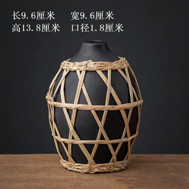 Black vase with woven straw cover on a wooden surface and dark background