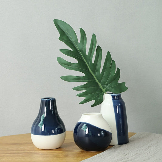 Three decorative vases with a plant leaf on a wooden surface against a plain background